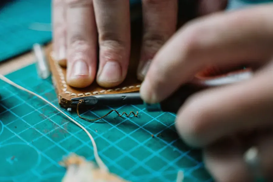 Hands stitching brown leather on a cutting mat